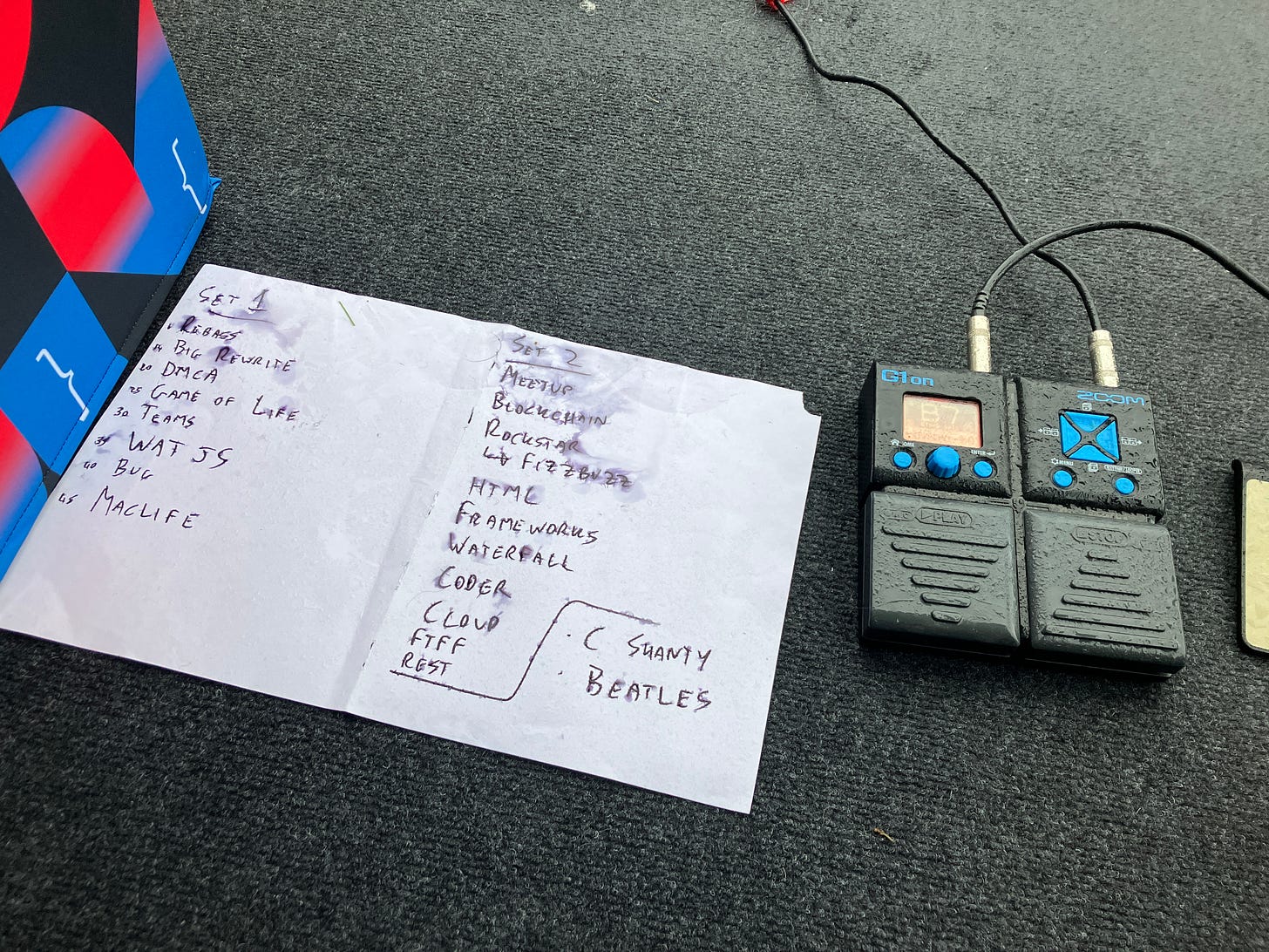 A handwritten set list next to a Zoom G1on guitar pedal. Both are soaked with rain.
