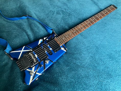 An image gallery showing a headless guitar being stripped down, sanded, repainted, and reassembled. By the end, it's blue with black and white stripes, and looks extremely shiny.
